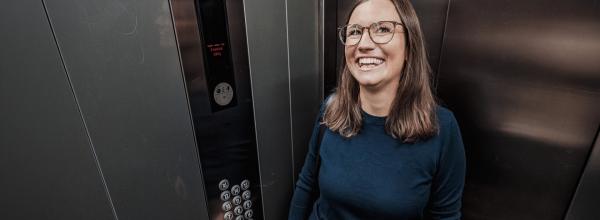 Frau steht lächenlnd in einem Aufzug