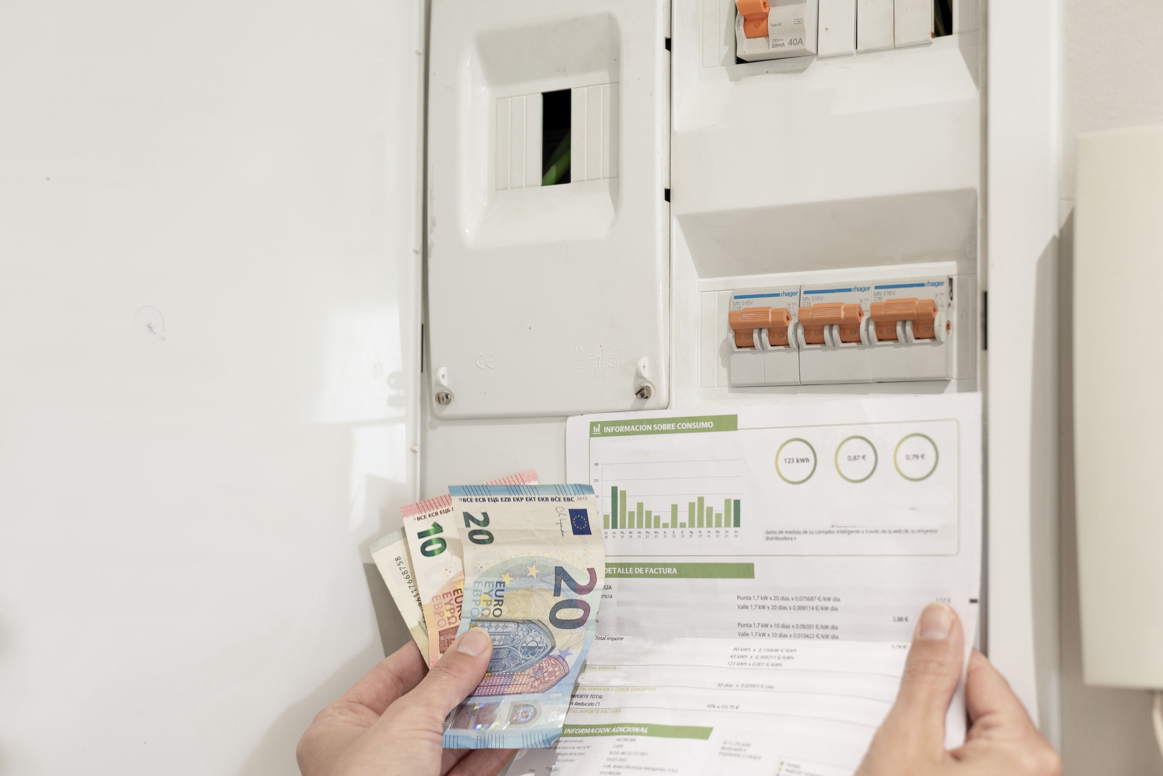 eine Hand, die die Stromrechnung und die Euro-Banknoten vor dem Netzschalter hält