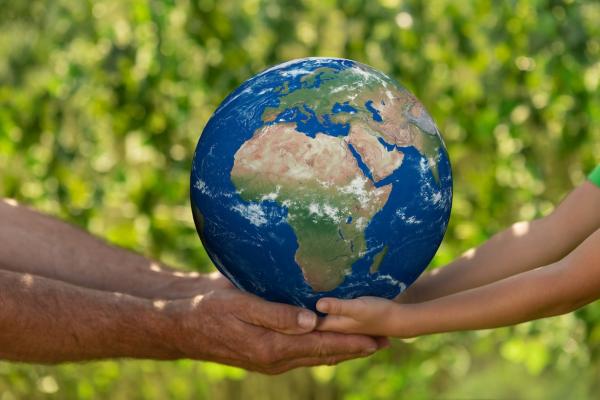 Männerhände und Kinderhände halten eine ERde-Symbol